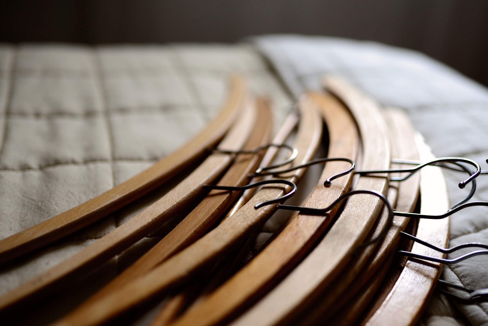 A pile of ten wooden hangers lay on a beige quilt.