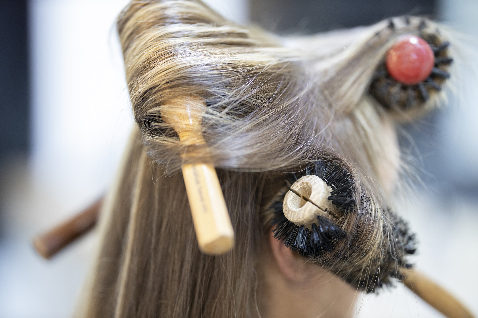 Close up of the side of woman's head. She has long, blonde, shiny hair and there are several hair brushes styling it.