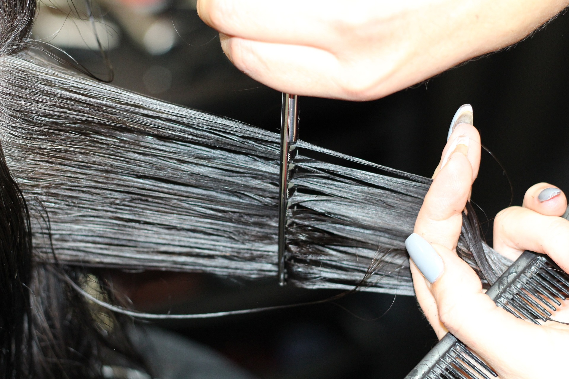 Close up of long, dark, wet hair being held and cut by a hair stylist.