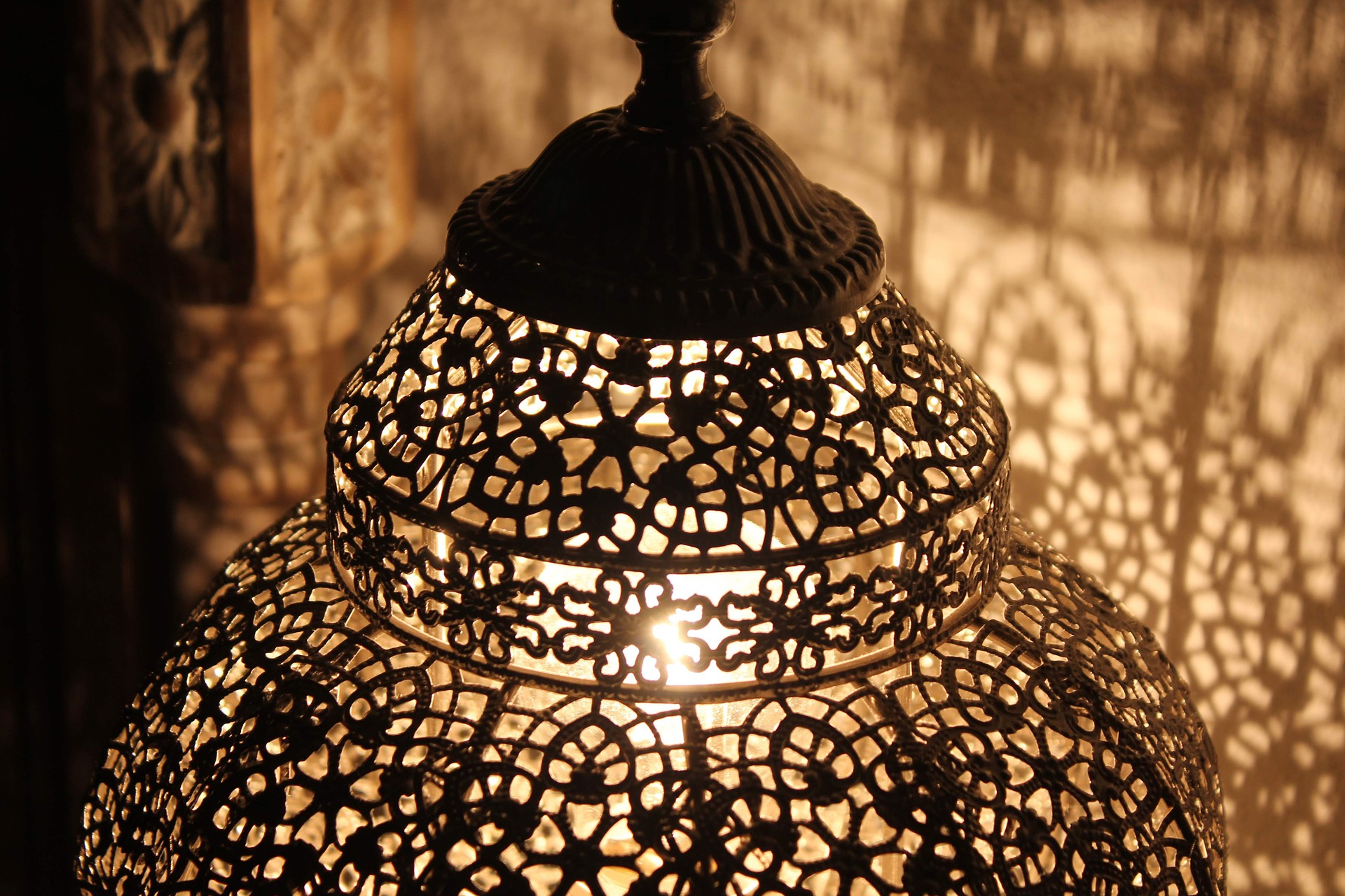 A Moroccan lantern with ornate perforations through from within which a cosy light shines and glows and creates a pattern in shadow on the wall
