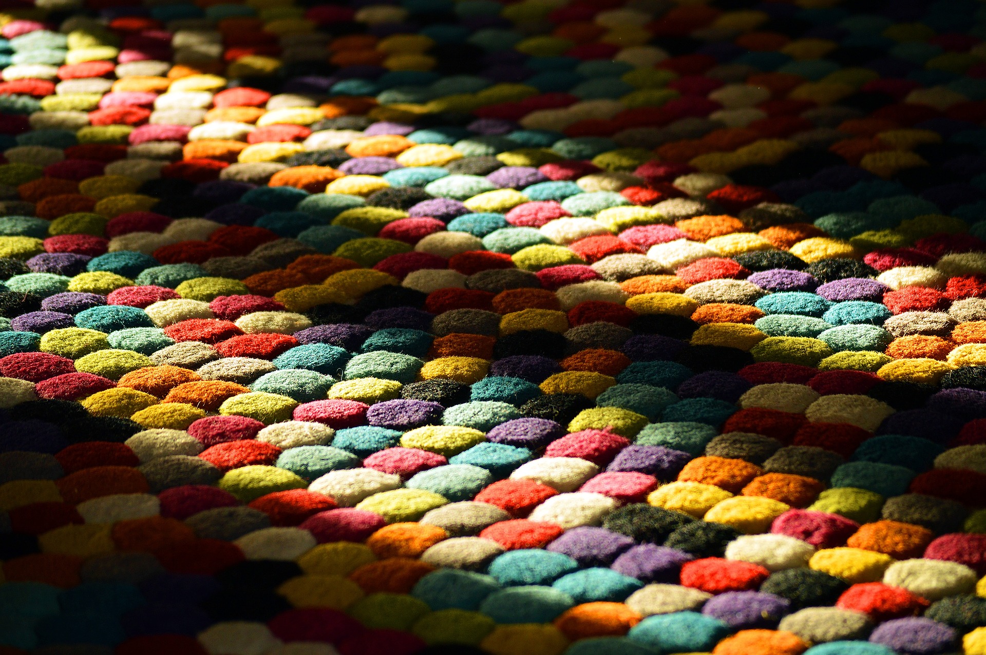 A close up of a thick rug made up of textured circles in all different colours. Shafts of sunlight are reflected on it